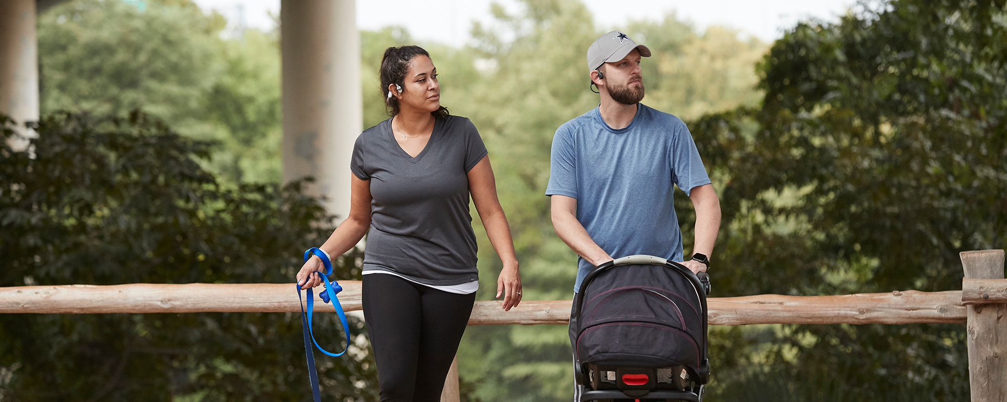 Man and woman walking with dog and child in stroller while wearing AfterShokz Aeropex headphones