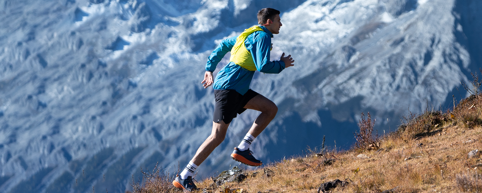 Image of a man running uphill on a mountainside while wearing Shokz OpenRun Pro wireless headphones