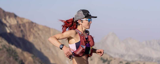 Professional Trail Runner & Coach Amanda Basham wearing weighted vest and running down mountainside while wearing OpenRun Pro headphones