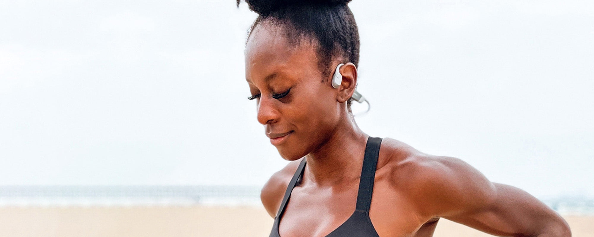 Close-up image of athlete Millie Sam-Otuh on a beach while wearing Shokz OpenRun wireless headphones