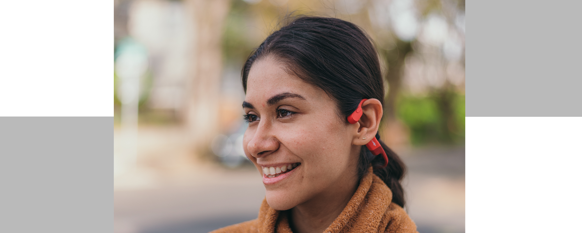 Close up image of a Latina woman smiling and wearing Shokz OpenRun headphones