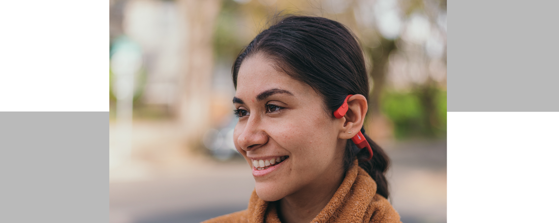 Close up image of a Latina woman smiling and wearing Shokz OpenRun headphones