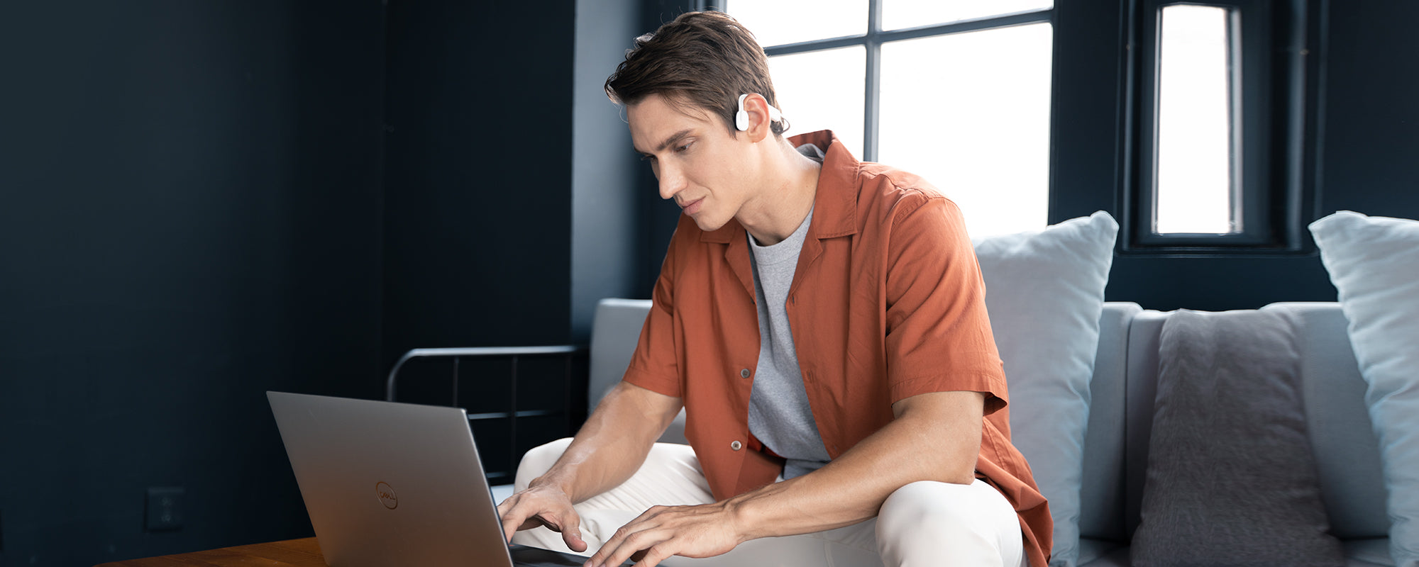 Man using laptop while wearing AfterShokz OpenMove headphones