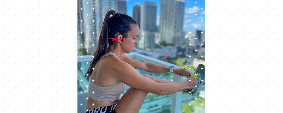 Woman standing on balcony doing leg stretches while wearing Shokz OpenRun wireless headphones