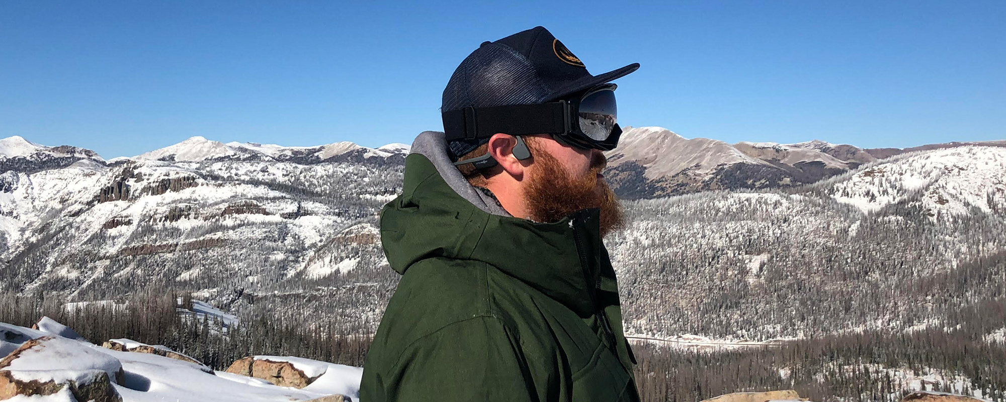 Man on snowy mountaintop wearing Shokz OpenRun headphones